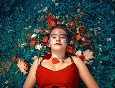 一个女人躺在绿色的草坪上，身上有五颜六色的花瓣